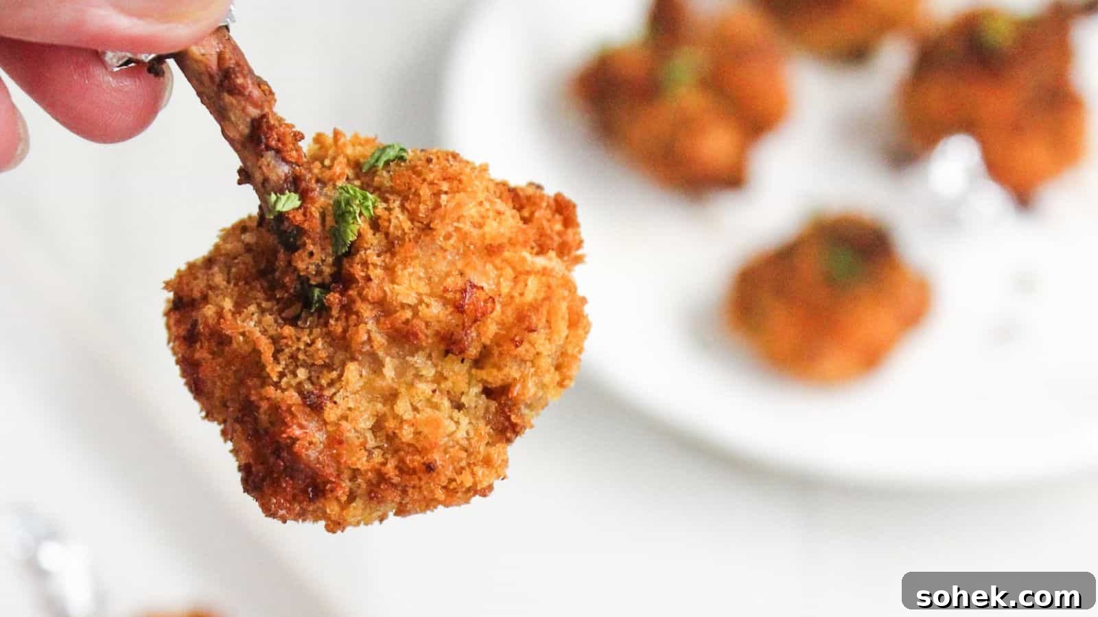 26 Irresistible Air Fryer Game Day Snacks to Serve Guests 9 A close-up of a hand holding a crispy breaded chicken drumstick, with more drumsticks on a white plate in the background.