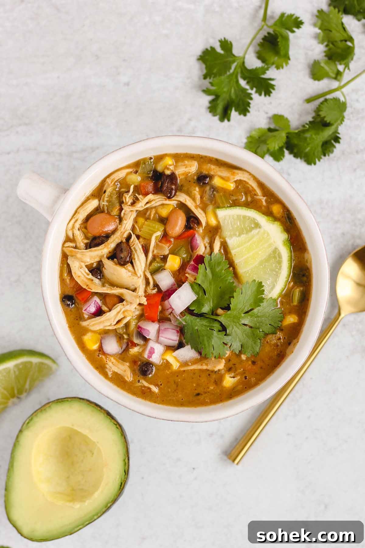 Southwestern Chicken Chili Recipe: Zesty One-Pot Dinner 10 Bowl of chicken chili topped with fresh cilantro and a lime wedge with a gold spoon and avocado half on the side.