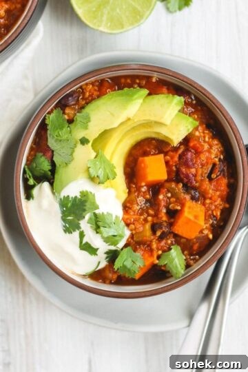 Vegetarian sweet potato topped with avocado, cilantro, and sour cream in a dark bowl sitting on a white plate.