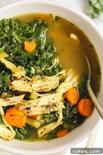 Chicken and kale soup in a white soup bowl with a spoon.