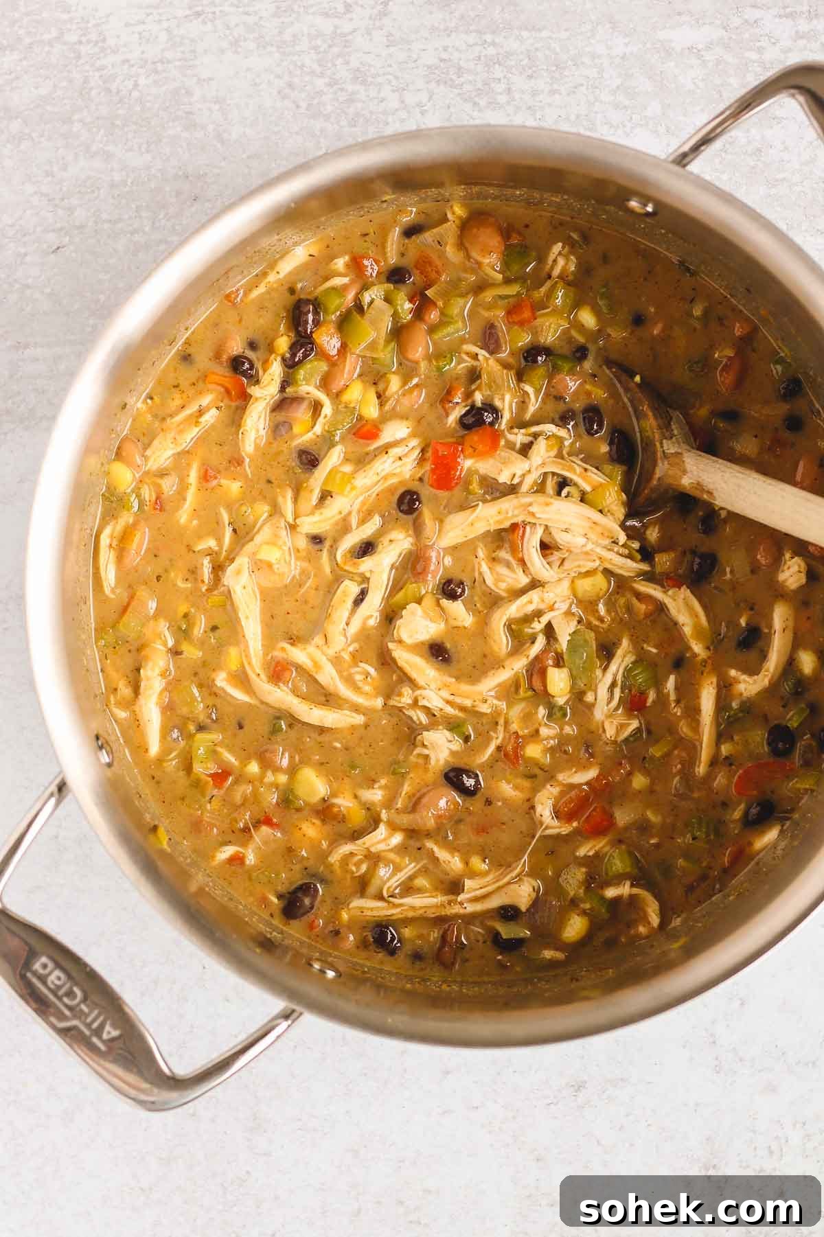 Southwestern Chicken Chili Recipe: Zesty One-Pot Dinner 8 Wooden spoon stirring fully made southwest chicken chili in a stainless steel pot.
