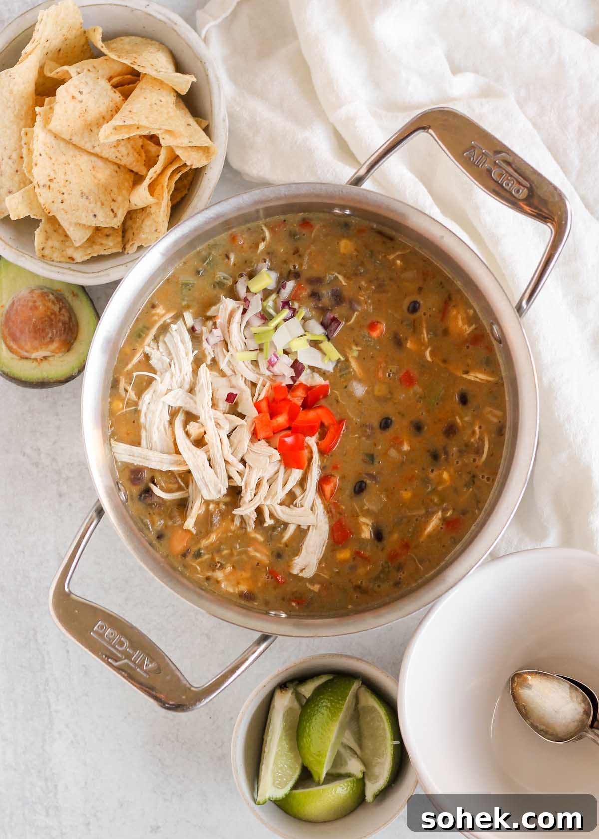 Southwestern Chicken Chili Recipe: Zesty One-Pot Dinner 9 Stainless steel stock pot full of chicken chili with bowls, lime wedges, avocado, and chips on the side of the pot.