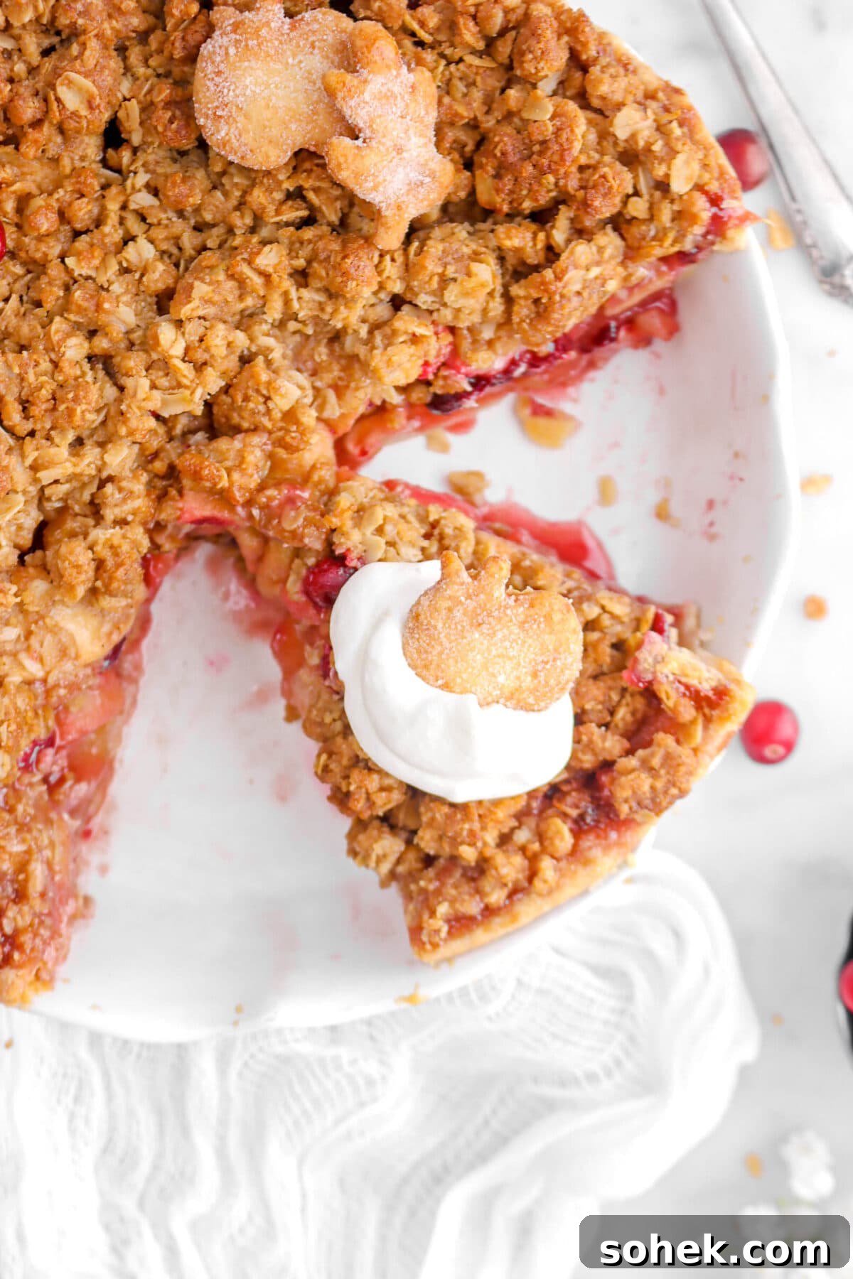 Apple Cranberry Crumble Pie Recipe with Buttery Oat Topping 17 overhead close up of slice of pie with a dollop of whipped cream and pie crust cut like an apple on top.
