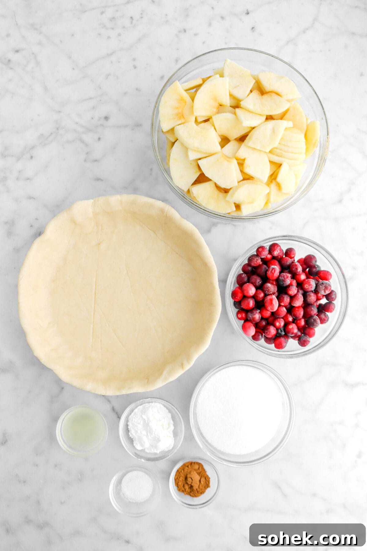 Apple Cranberry Crumble Pie Recipe with Buttery Oat Topping 6 sliced apples, unbaked pie crust, cranberries, sugar, cinnamon, cornstarch, salt, and lemon juice on marble surface.