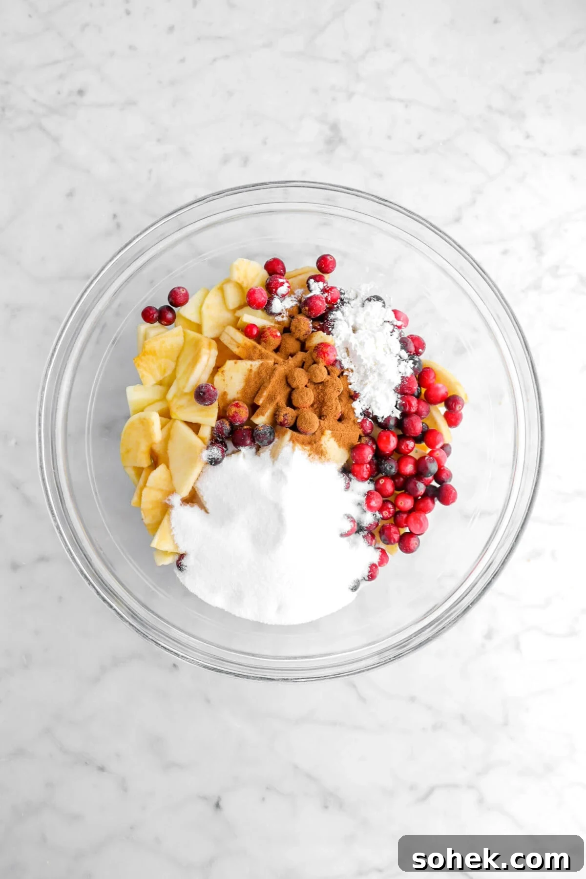 Apple Cranberry Crumble Pie Recipe with Buttery Oat Topping 8 sugar, cinnamon, cranberries, and sliced apples in glass bowl.