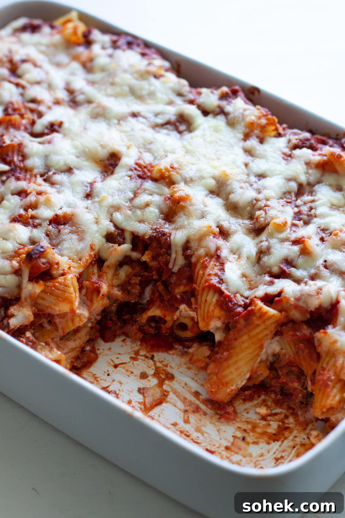 A baking dish with rigatoni al forno and a piece taken out of the pasta dish.