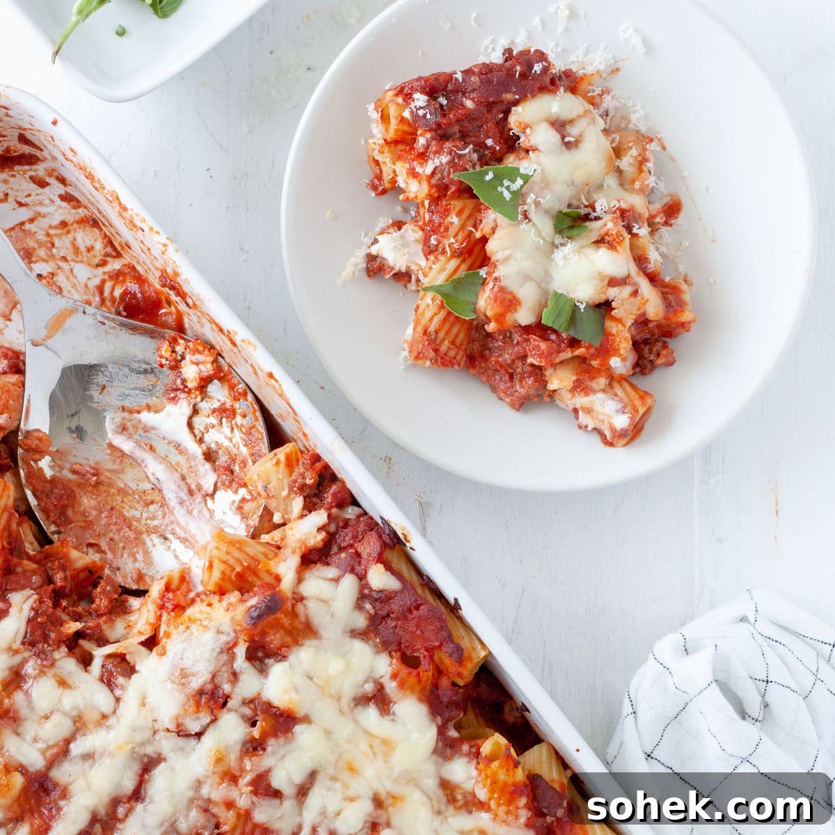 A scoop of rigatoni al forno taken out of a baking dish full of the baked pasta.
