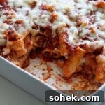 A baking dish with rigatoni al forno and a piece taken out of the pasta dish.