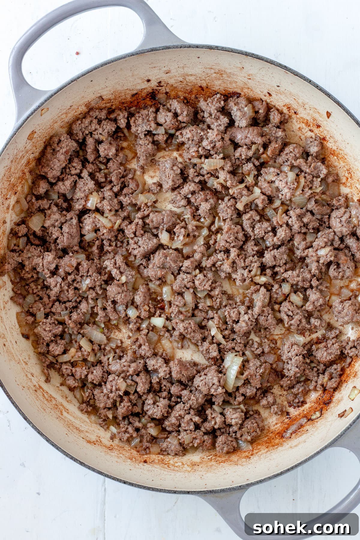 Ground beef and onions cooking in a large skillet.