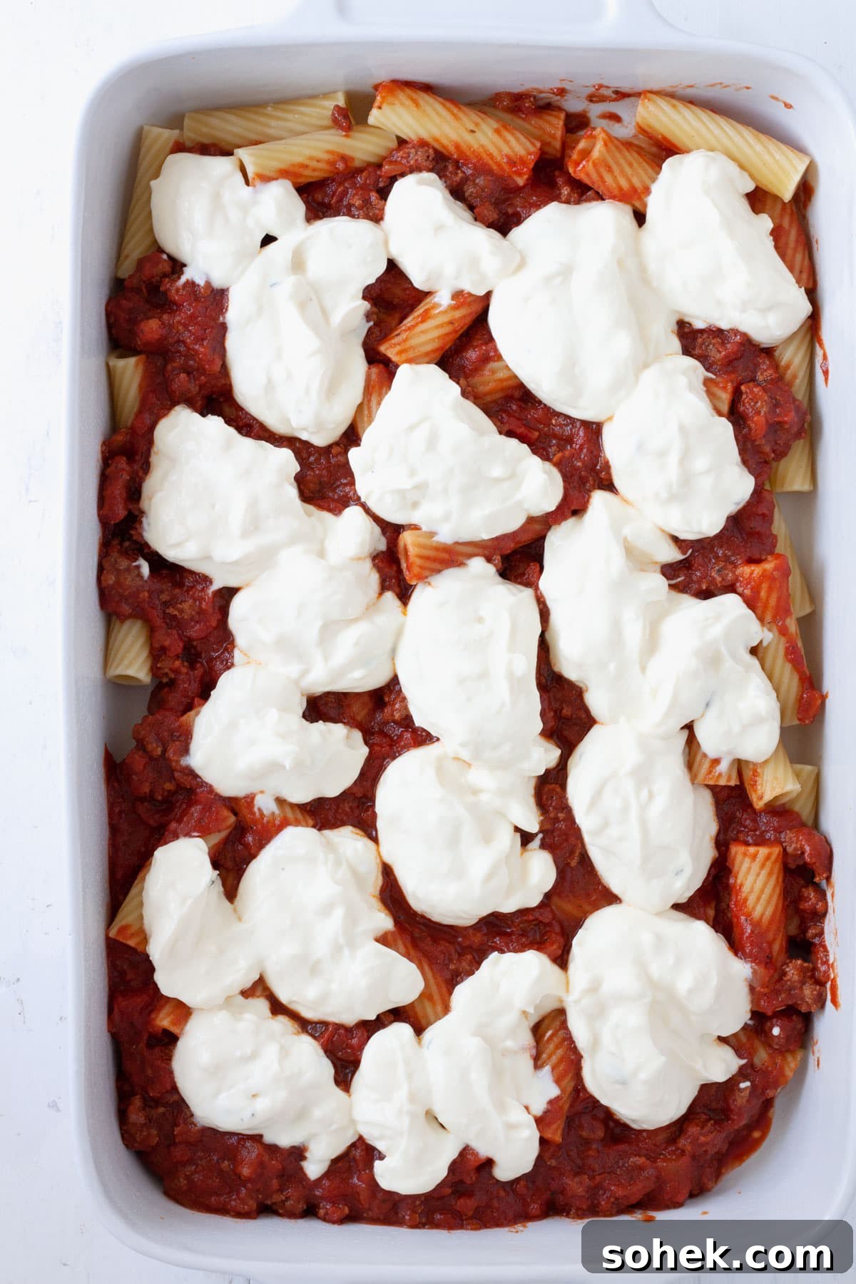 Ricotta dolloped on a partially assembled rigatoni al forno.