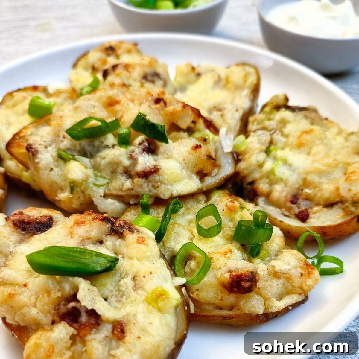 Stuffed potato skins garnished with chopped spring onions on a white plate.