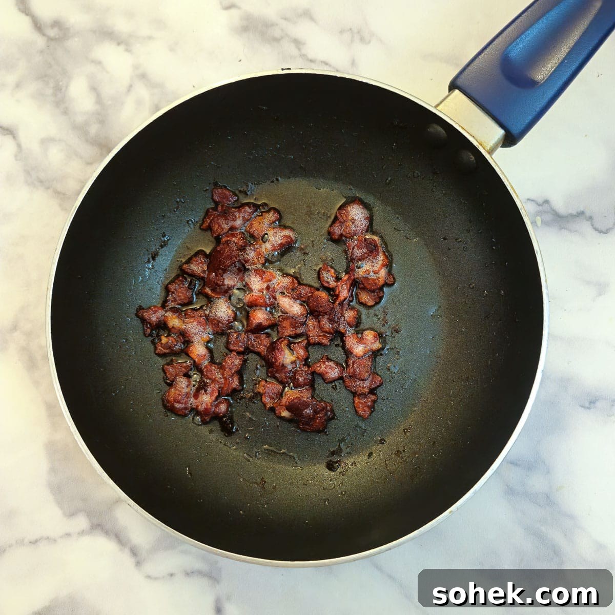 Bacon pieces frying in a black frying pan.