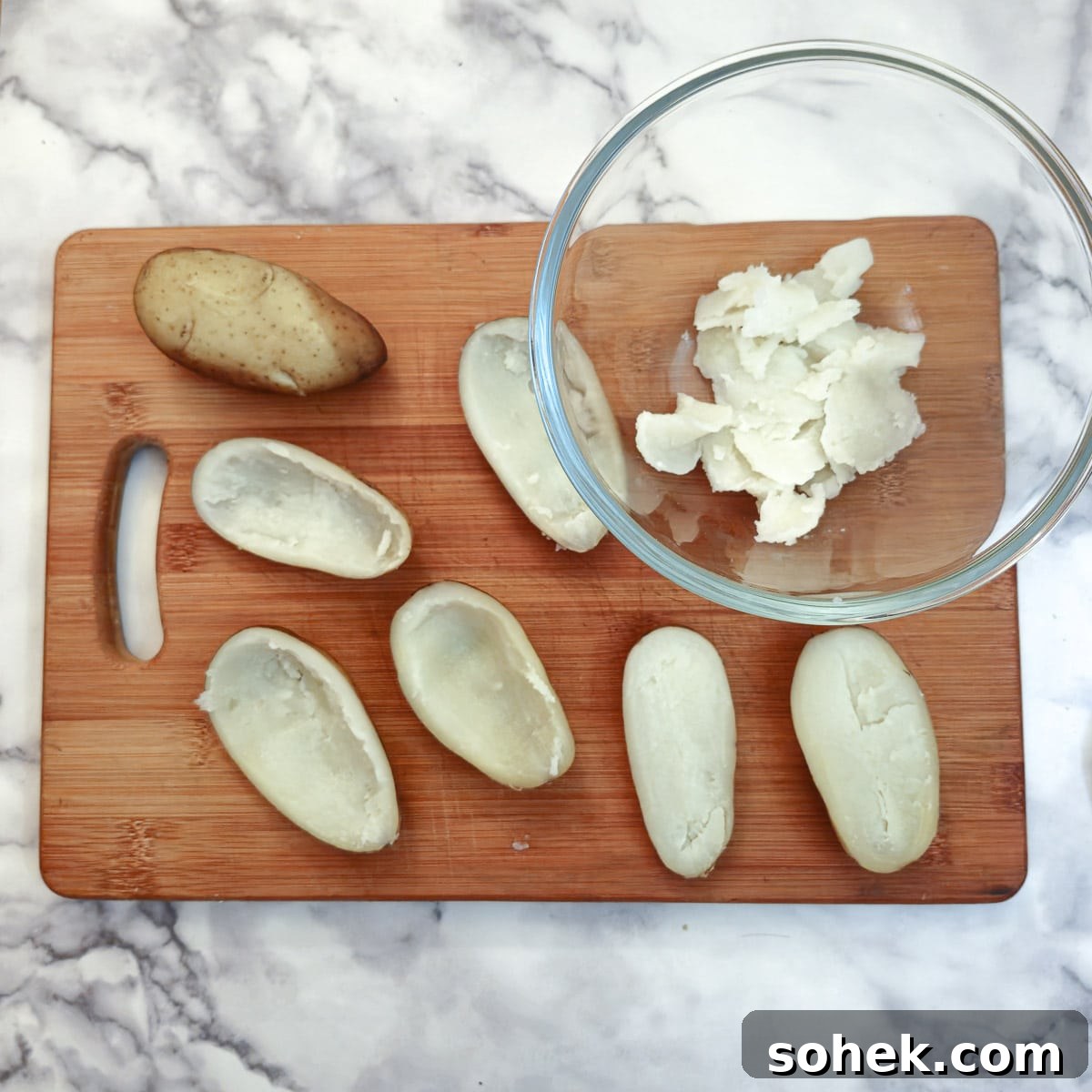 Baked potatoes cut in half with the insides scooped into a bowl.
