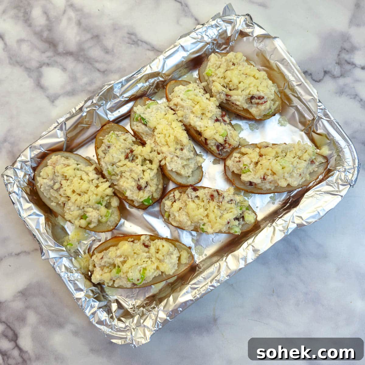 Potato skins stuffed with filling and covered with grated cheese on a baking tray.
