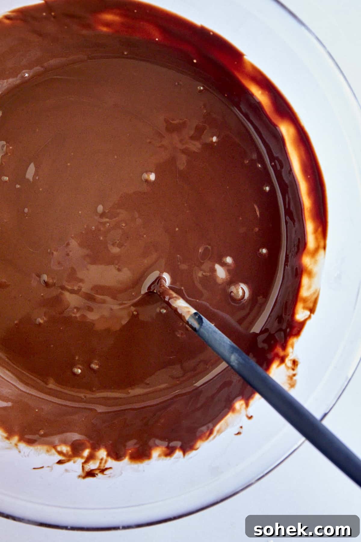 Viral Chocolate-Covered Strawberry Yogurt Clusters Recipe 4 A bowl of melted chocolate and coconut oil with a spoon sticking out.