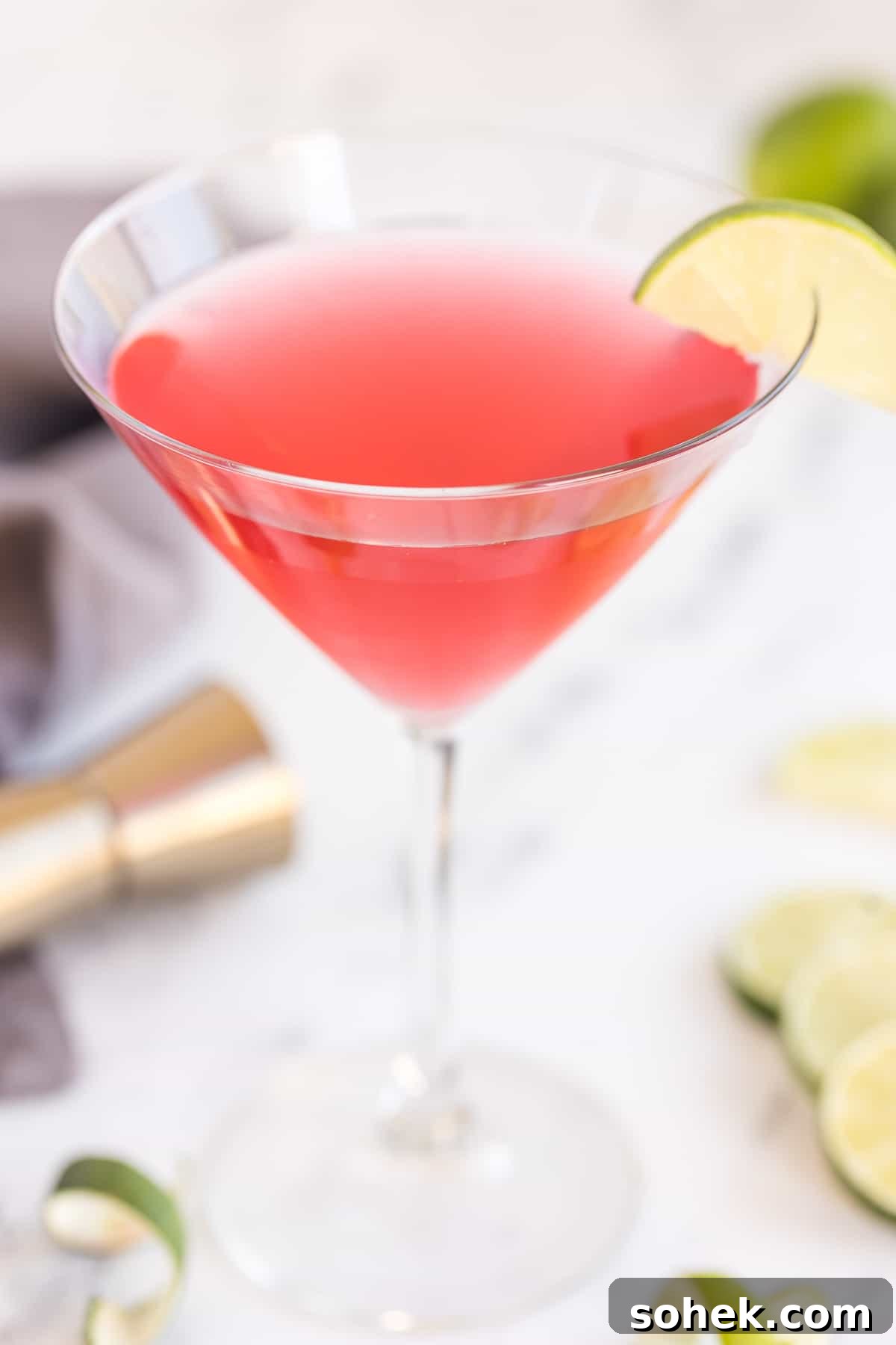 Classic Cosmopolitan Cocktail Recipe: How to Mix a Perfect Cosmopolitan 2 A cosmopolitan cocktail in a martini glass with a slice of lime on the rim on a kitchen counter.