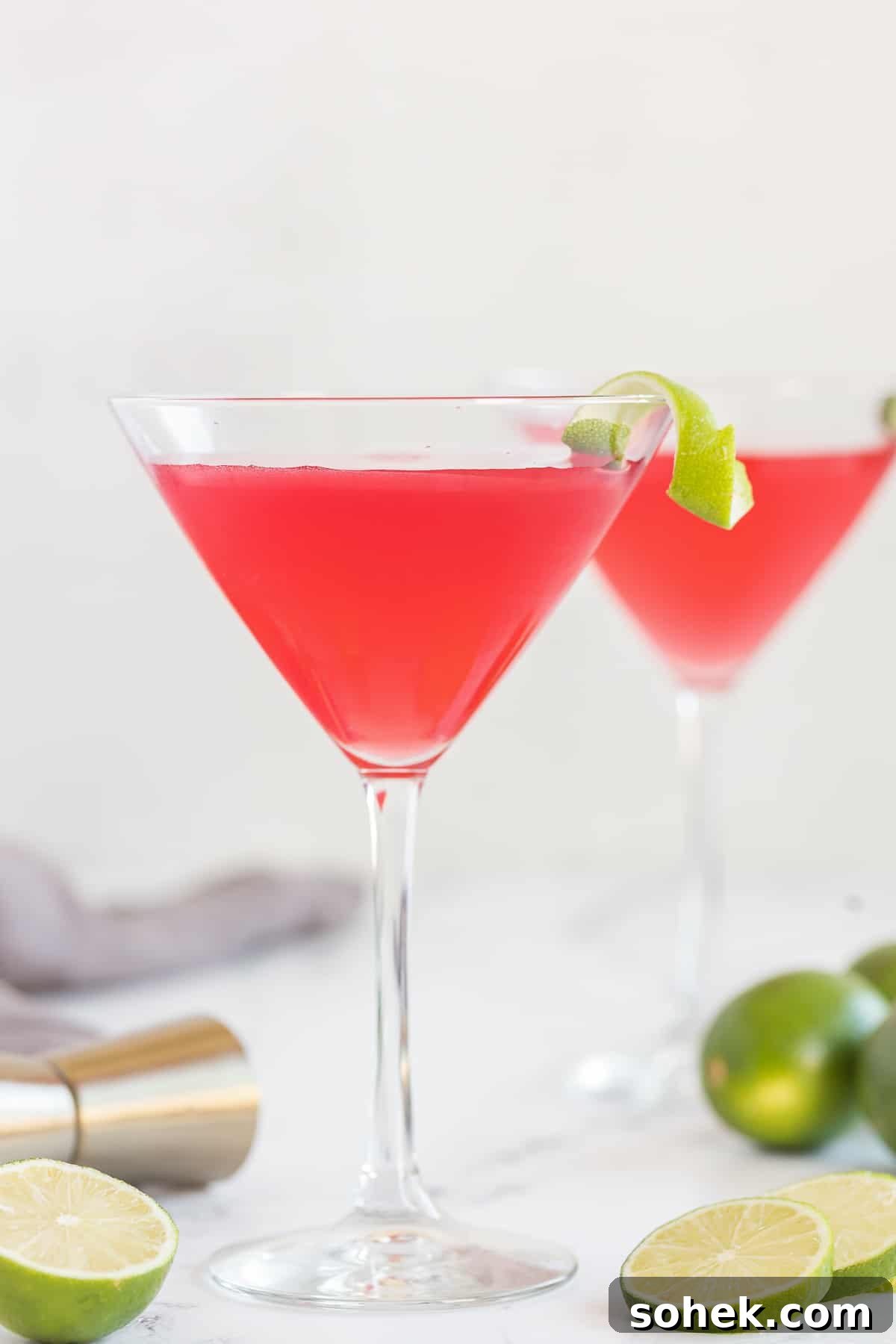 Classic Cosmopolitan Cocktail Recipe: How to Mix a Perfect Cosmopolitan 10 Two cosmos in martini glasses garnished with a twist of lime on the rim.