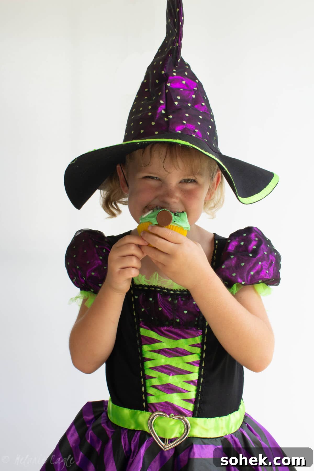little girl wearing a witch costume for halloween eating a halloween cupcake