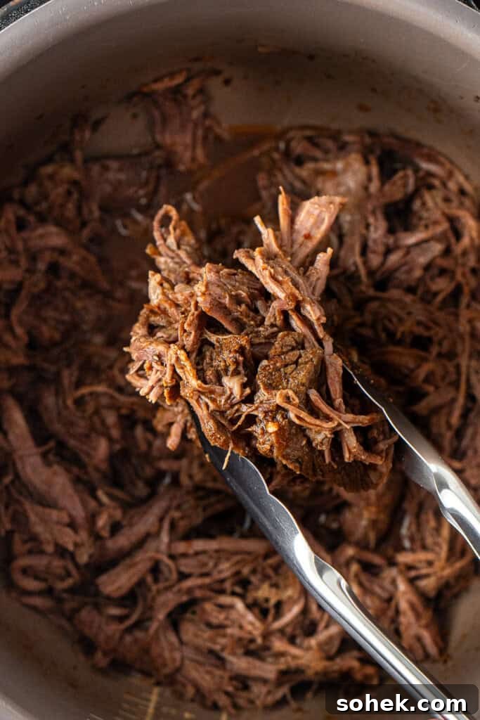 Shredded beef being held up with tongs.
