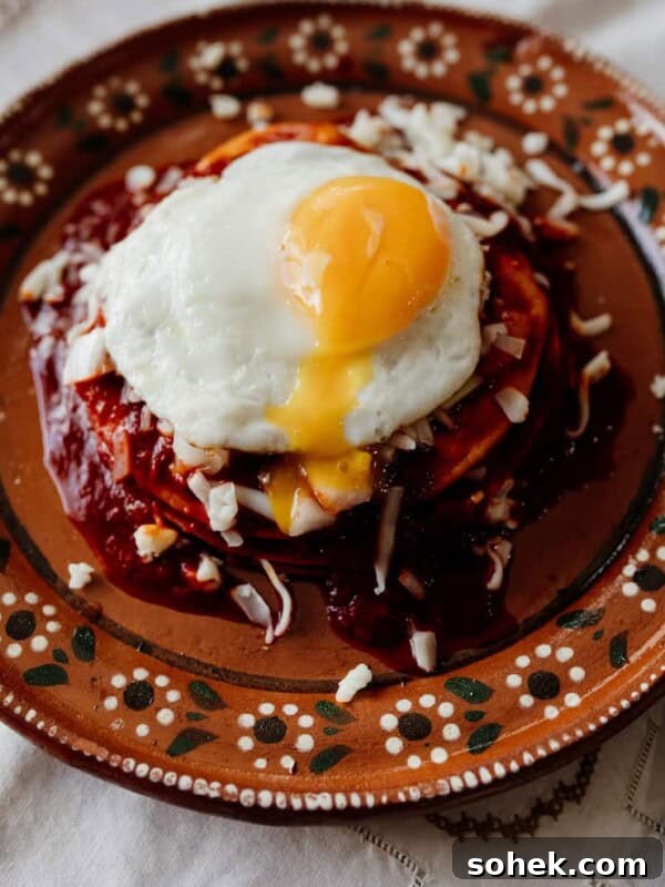 stacked red enchiladas on an earthenware plate with a fried egg on top