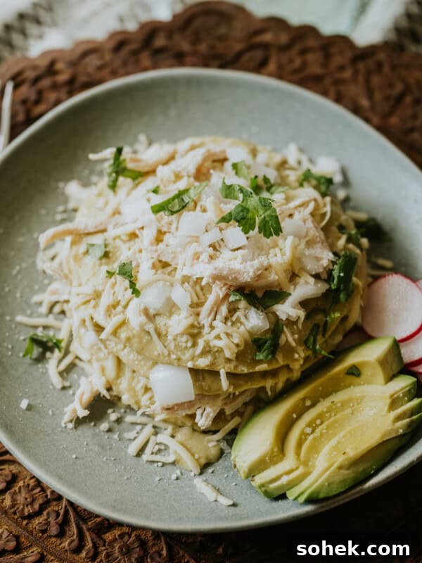Stack of enchiladas verdes layered with shredded chicken, shredded white cheese, and a creamy roasted green chile sauce, and garnished with cilantro.