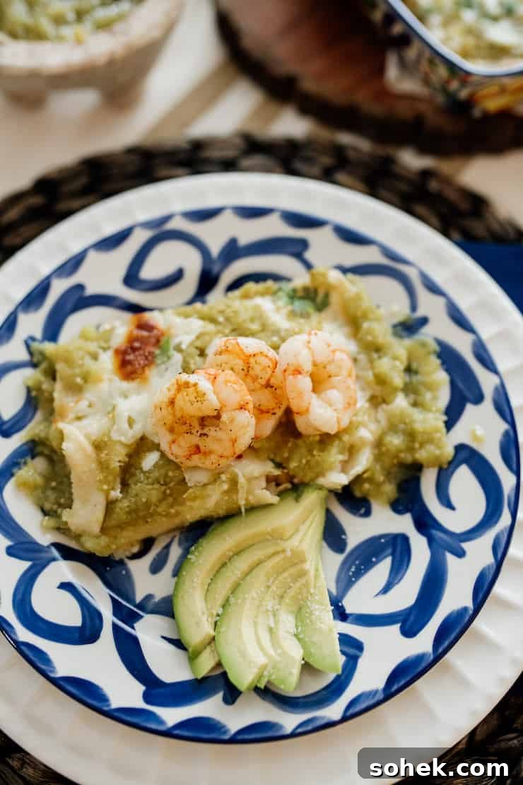 a serving shrimp enchiladas in a salsa verde with a side of slices of avocado. 
