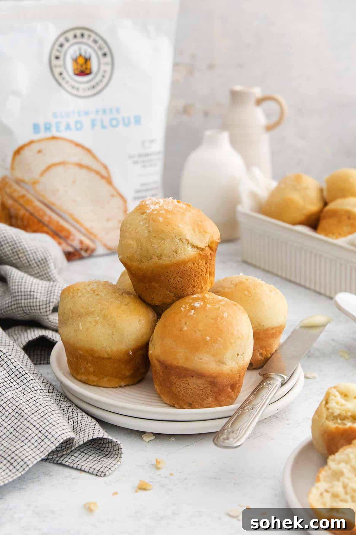 Soft Gluten-Free Dinner Rolls Recipe for Tender, Fluffy Buns 3 dinner rolls stacked on a plate with a butter knife.