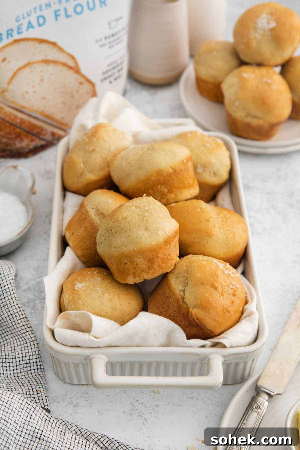 Soft Gluten-Free Dinner Rolls Recipe for Tender, Fluffy Buns 9 dinner rolls in a white baking dish with a tea towel.