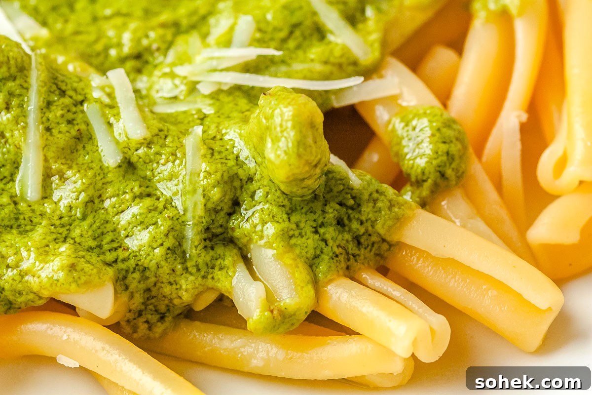 A close-up shot of hot pasta coated in green lemon pesto sauce and sprinkled with freshly grated Parmesan cheese.