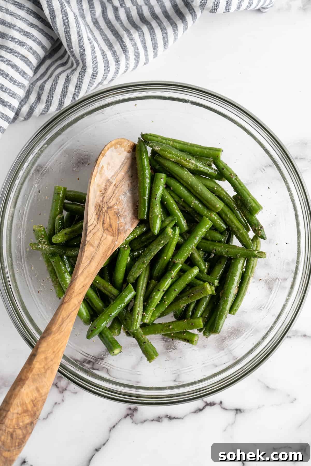 These air fryer green beans are seasoned to perfection and air fried until crispy for an easy side dish that goes with anything! Green beans in glass bowl with wooden spoon.
