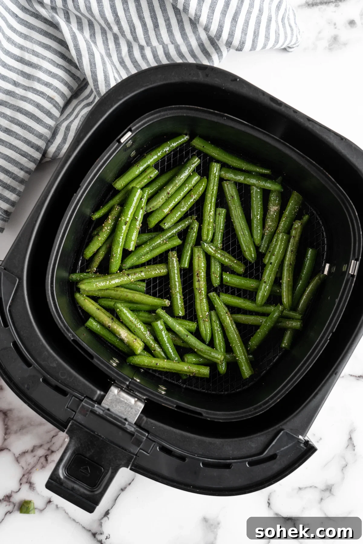 These air fryer green beans are seasoned to perfection and air fried until crispy for an easy side dish that goes with anything! Green beans in air fryer basket.
