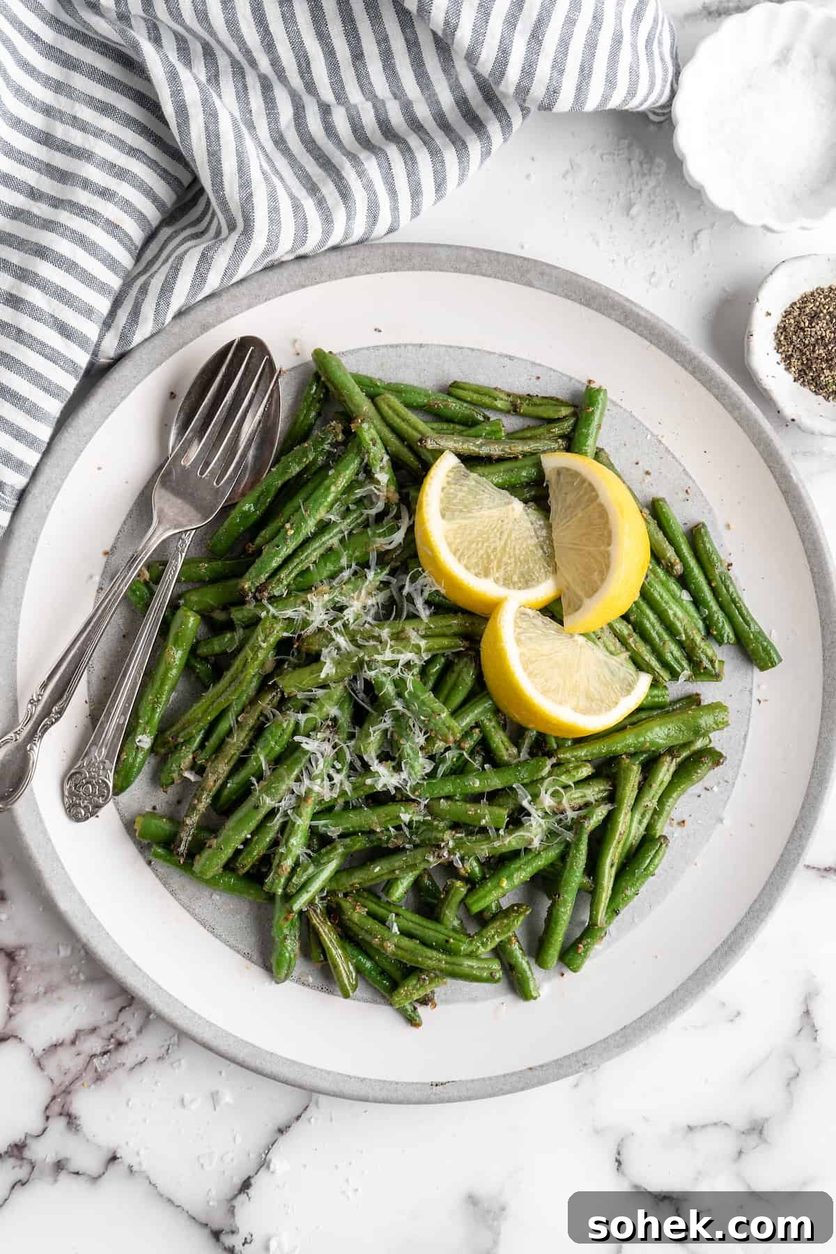 These air fryer green beans are seasoned to perfection and air fried until crispy for an easy side dish that goes with anything! Overhead view of air fryer green beans on plate with spoon, fork, and lemon wedges.