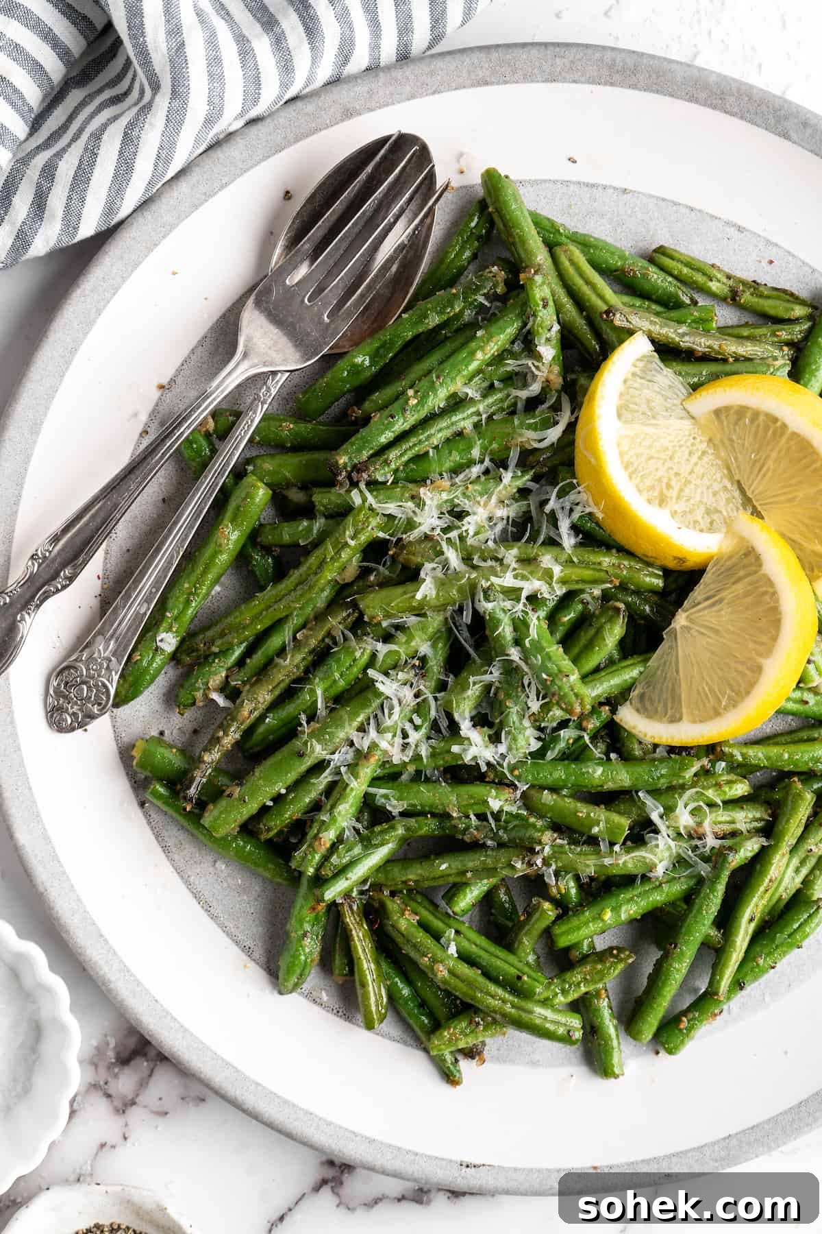 These air fryer green beans are seasoned to perfection and air fried until crispy for an easy side dish that goes with anything! Air fryer green beans on plate with spoon, fork, and lemon wedges.