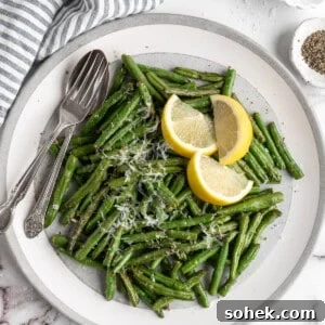 Crispy Air Fryer Green Beans with Garlic and Parmesan 2 Overhead view of air fryer green beans on plate with spoon, fork, and lemon wedges
