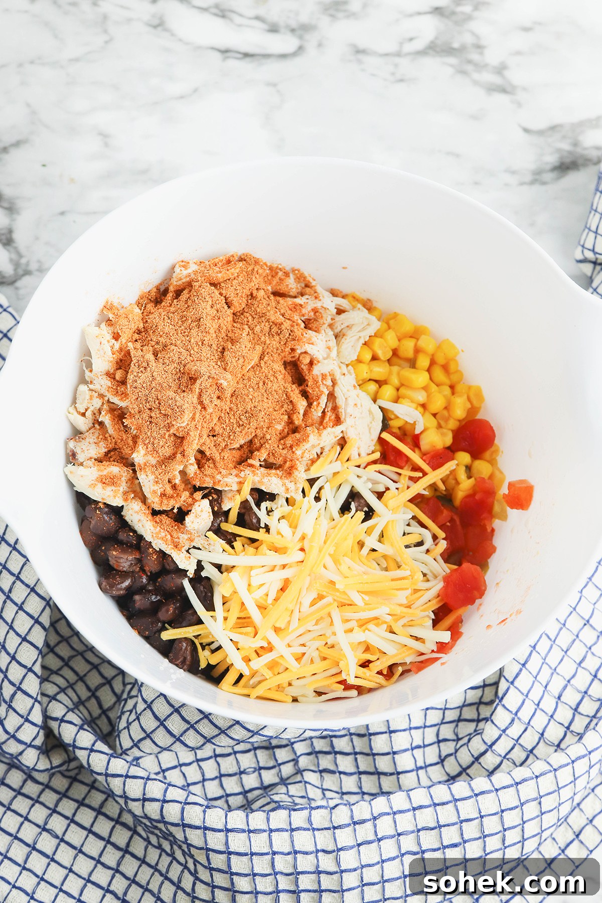 Shredded chicken, black beans, diced tomatoes, corn, and taco seasoning in white mixing bowl.