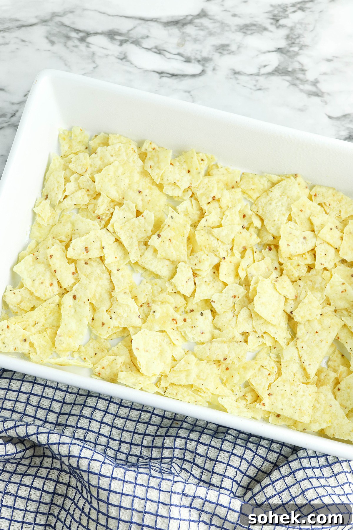 Layer of crushed tortilla chips in bottom of white baking dish.