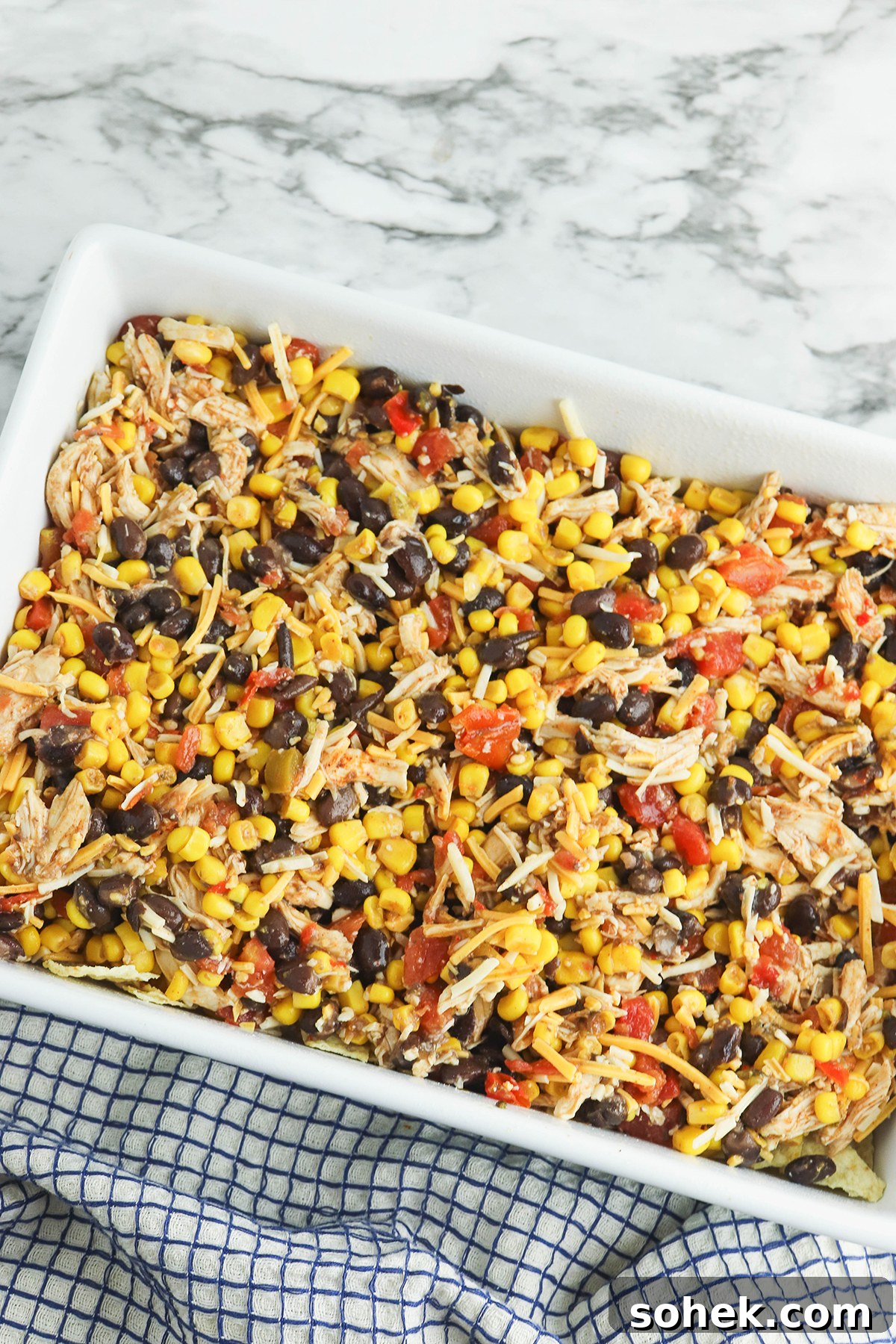 Mexican chicken mixture spread over bottom layer of crushed tortilla chips in white baking dish.