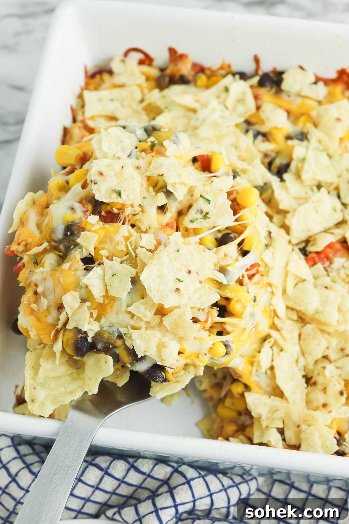 Spoon with a serving of Mexican Chicken casserole with tortilla chips over baking dish.