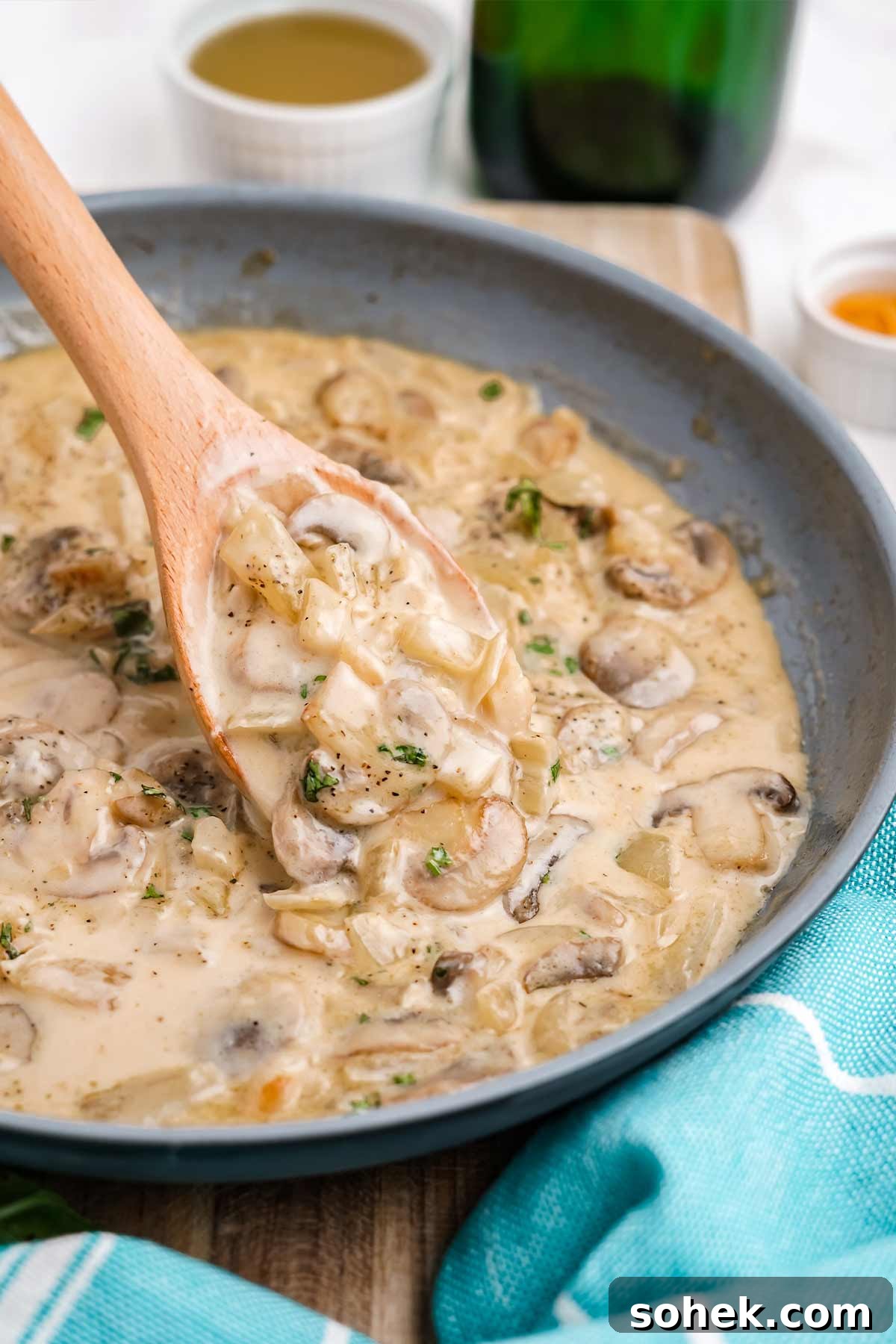 White wine mushroom sauce with cream in a skillet with a wooden spoon scooping some out.
