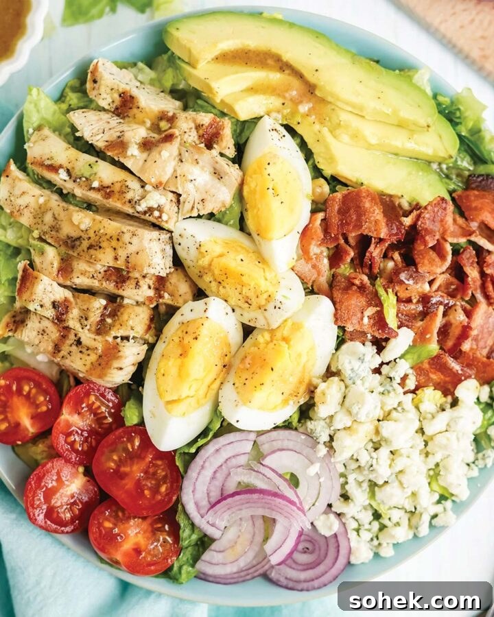 Cobb salad with chicken, eggs, avocado, tomatoes, blue cheese and onions in a blue bowl on the table.