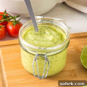 Mason jar with avocado ranch dressing on a wooden table. Tomatoes in white background.