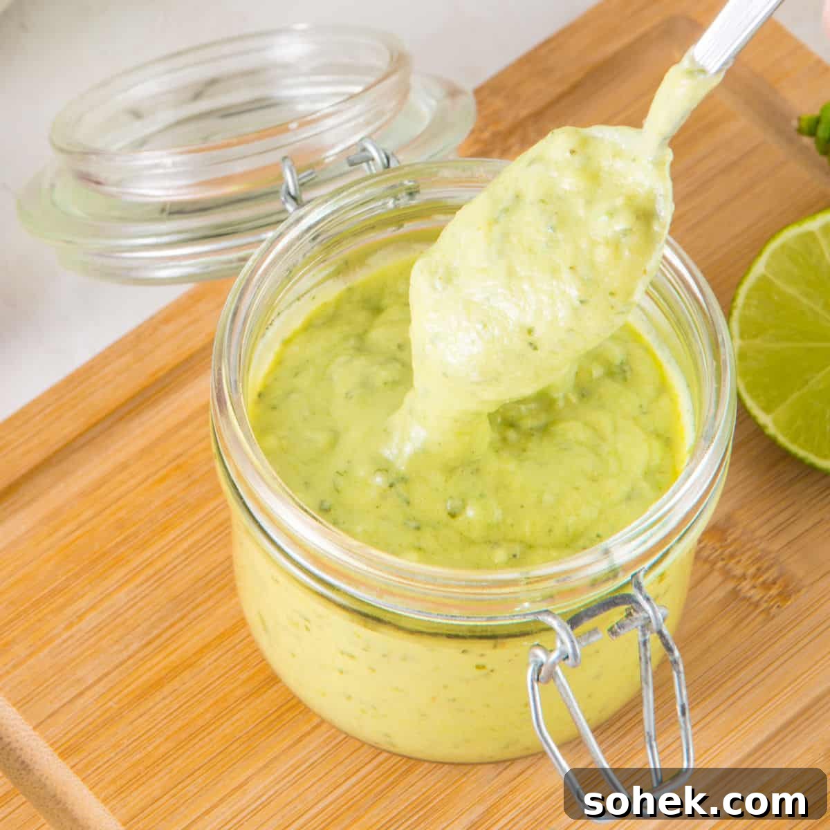 Spooning avocado lime dressing from a mason jar on a wooden board. 