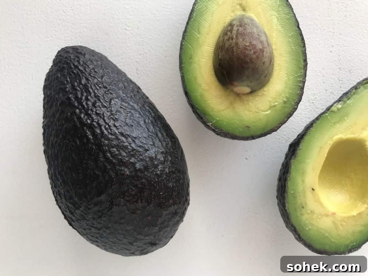 One whole avocado and two halved parts on a white surface.