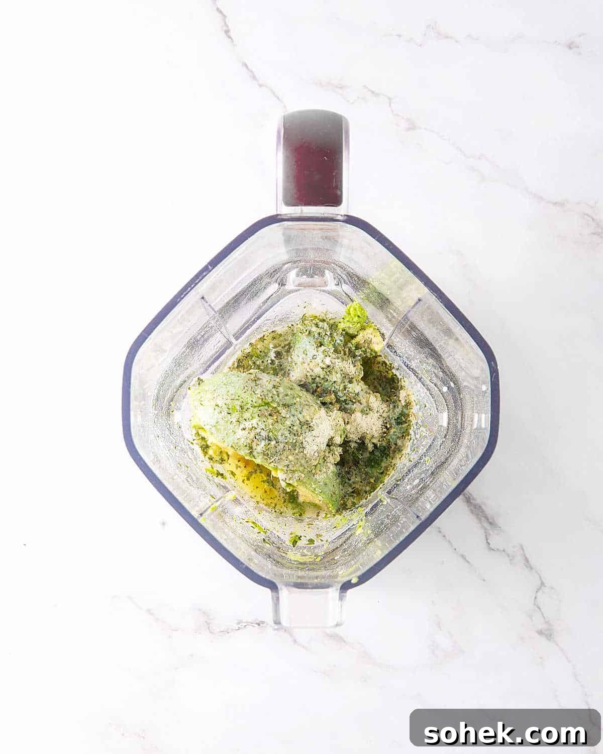 Top view of blender jar on white marbled surface with ingredients for avocado lime ranch dressing.