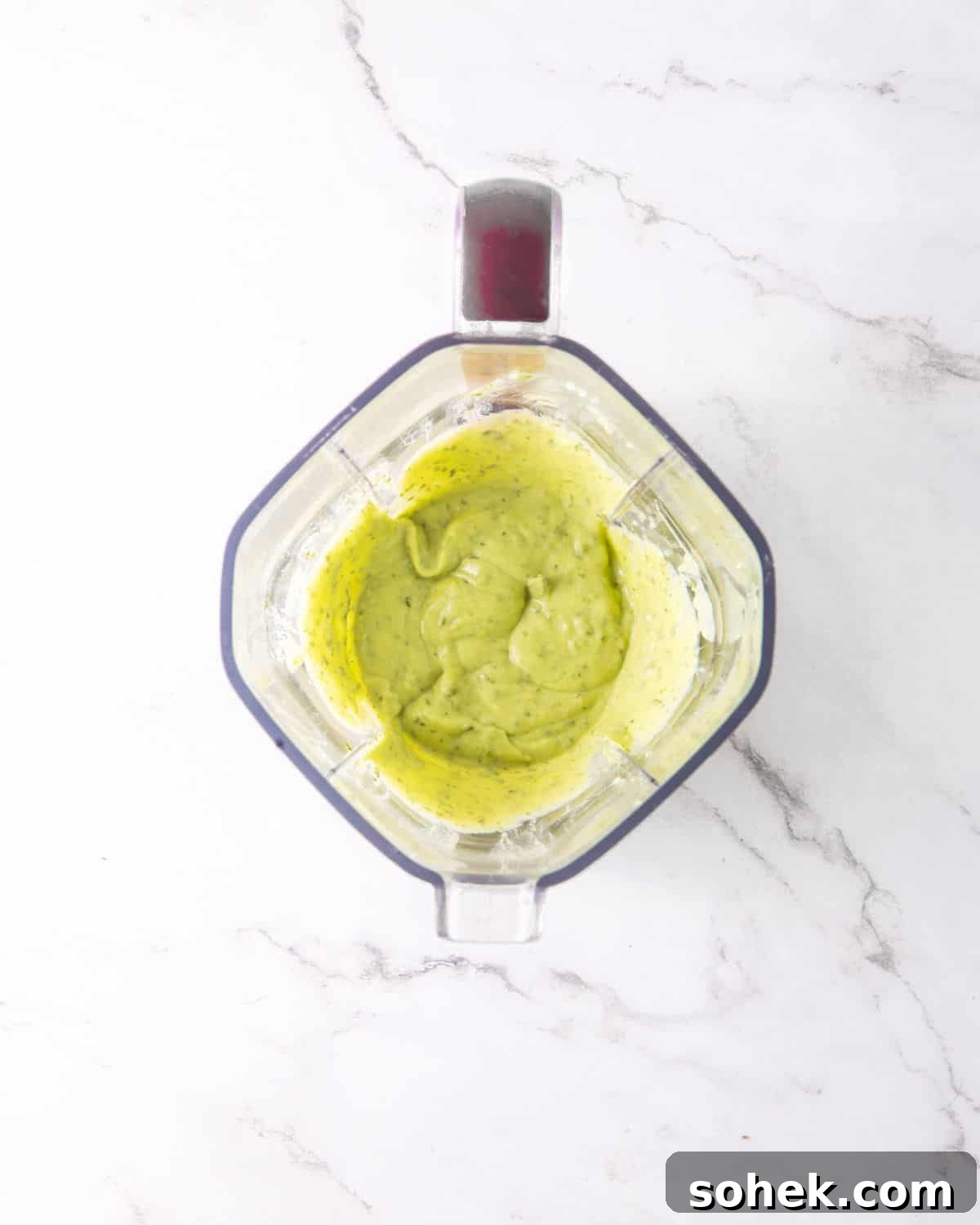 Blended avocado ranch dressing in the jar of a blender on a whit marbled surface.