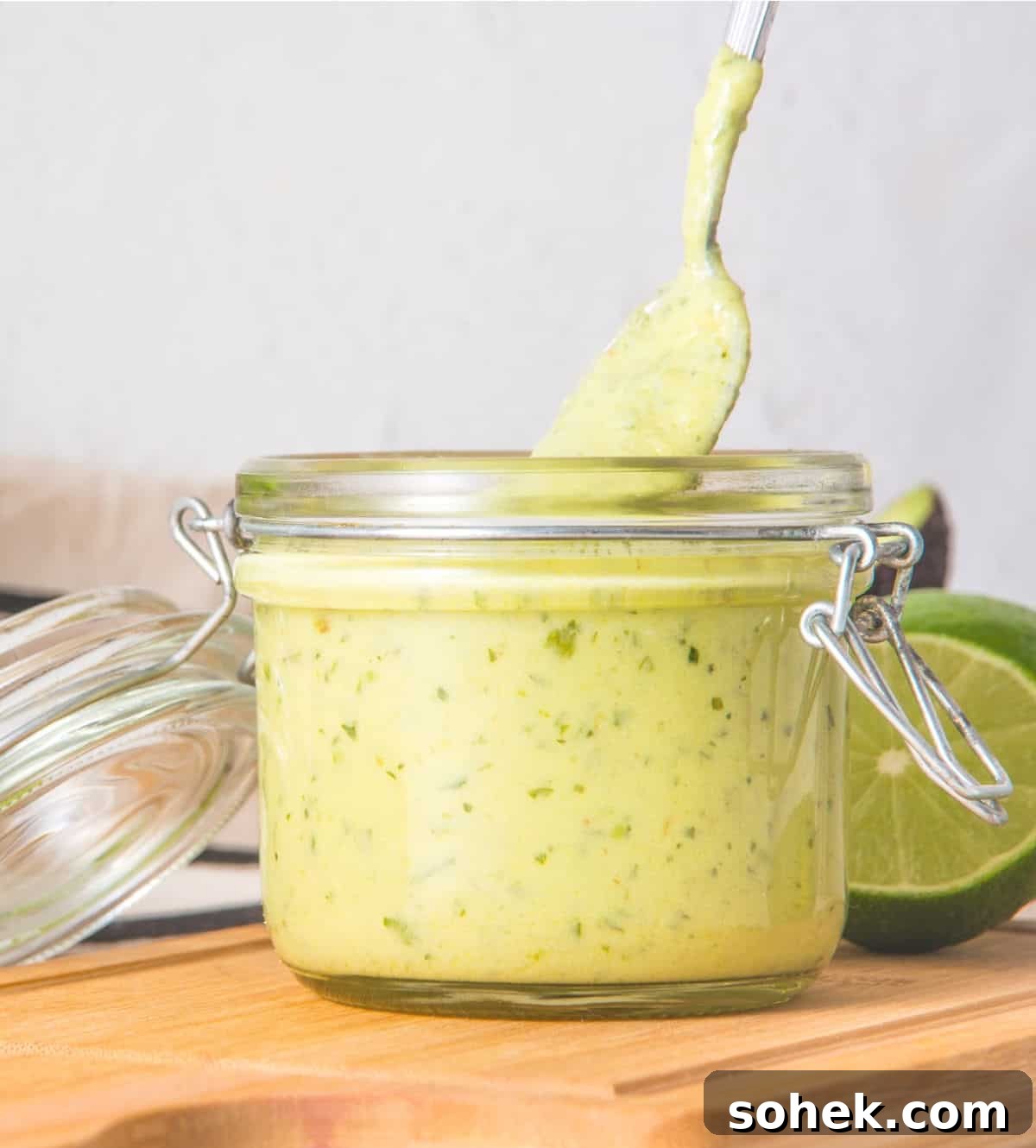 Lifting a spoon from a mason jar with avocado ranch dressing on a wooden board. 