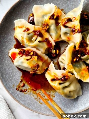 Close up of a plate of boiled dumplings drizzled in chilli oil dipping sauce