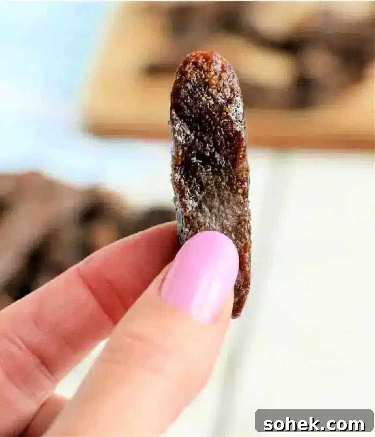 Crispy Air Fryer Beef Jerky Recipe for Homemade Snacks 2 A hand with pink nail polish holds a single dried tamarind piece close to the camera, reminiscent of air fryer beef jerky in its texture and appearance.