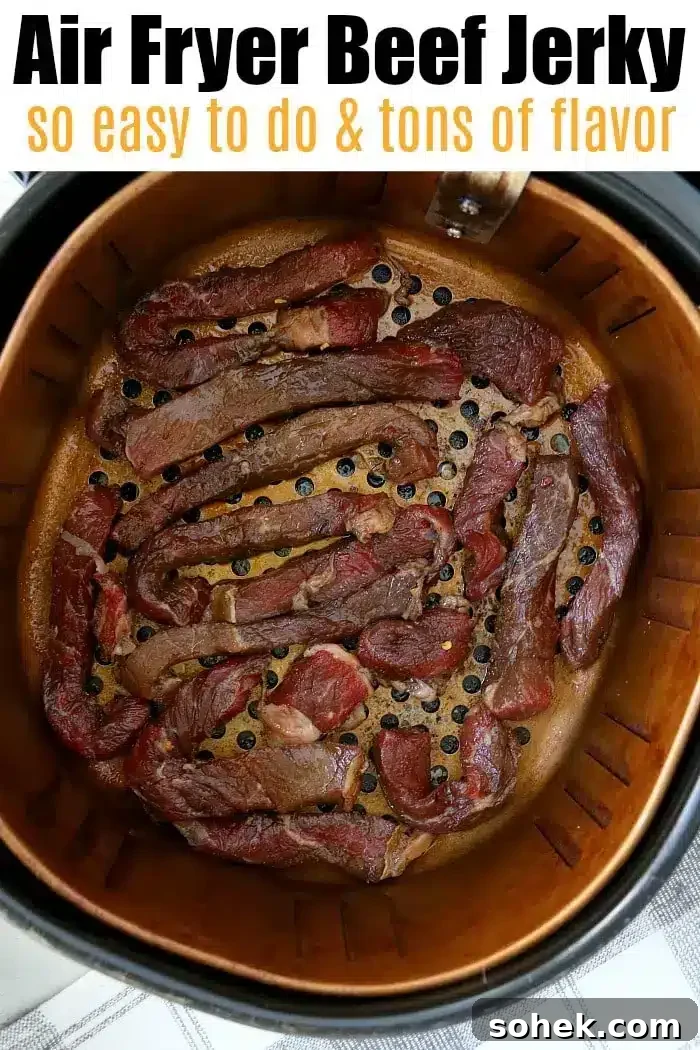 Crispy Air Fryer Beef Jerky Recipe for Homemade Snacks 5 A metal air fryer basket is filled with pieces of savory beef jerky. The top of the image contains text that reads: "Air Fryer Beef Jerky so easy to do & tons of flavor." The setup is on a gray-patterned countertop.