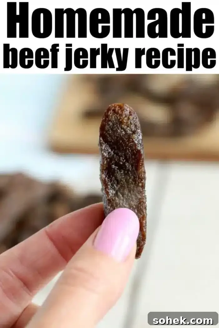 Crispy Air Fryer Beef Jerky Recipe for Homemade Snacks 8 A close-up of a hand with pink-painted nails holding a piece of beef jerky. "Homemade air fryer beef jerky recipe" is written in bold black letters at the top of the image. In the background, more pieces of jerky are spread out on a wooden surface.
